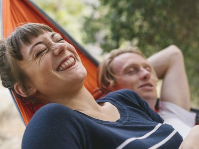 woman smiling sitting next to man with eyes closed in a hammock