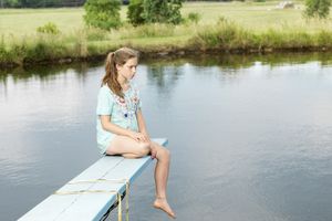 Unhappy girl sitting on a diving board over a pond