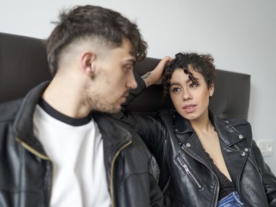 Man and woman having a serious conversation, sitting on a bedroom bed, dressed in casual clothes and staring at each other.