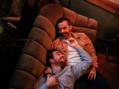 Two men snuggling on the couch, smiling at each other