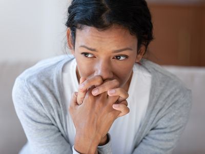 An anxious, fearful young woman clasps her hands in front of her face