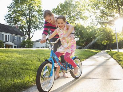 Babysitter teaching little girl how to ride a bike