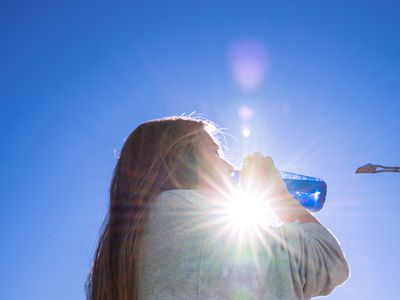 Blonde woman drinking water outside while being illuminated by a ray of sunlight.