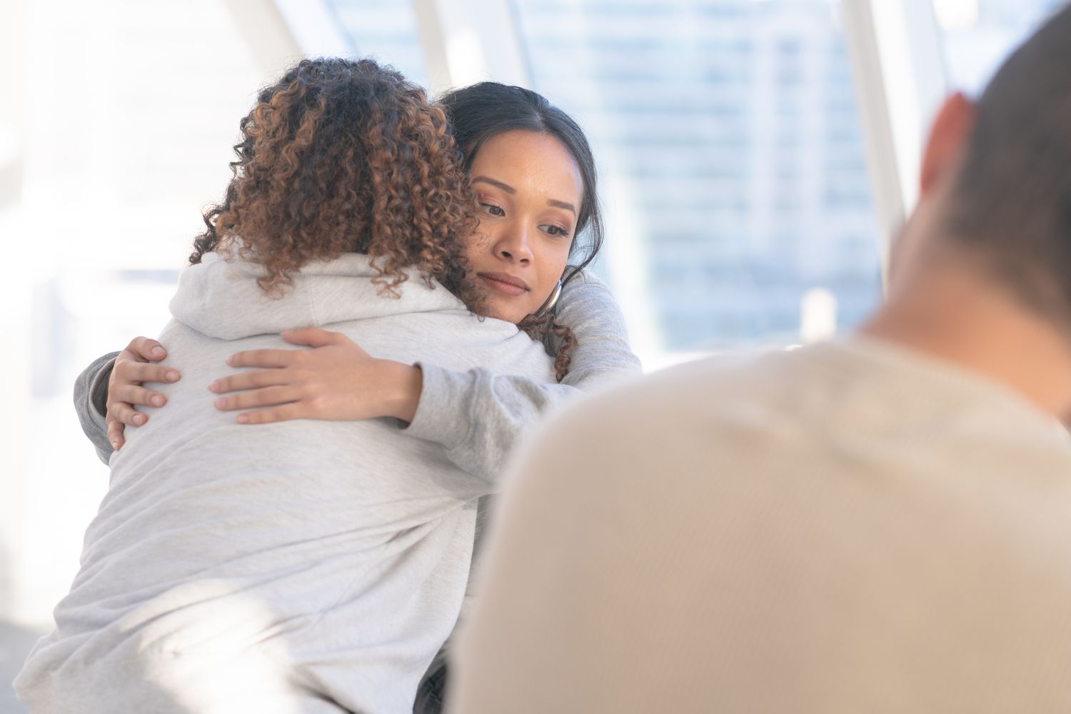 Two (2) women embrace in a comforting hug.