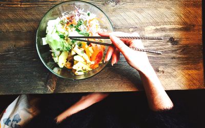 woman's hands holding chopsticks in bowl of food