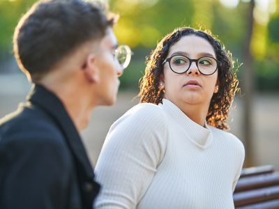 Young woman keeping distance and rejecting a man while having a date together outdoors in a park.