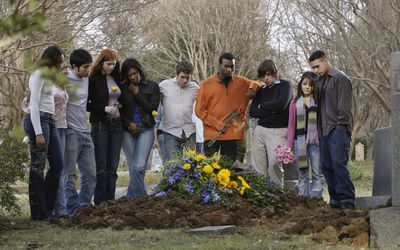 A group of young adults congregate around the grave of a friend who died from drugs