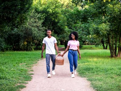 Young black couple walking with picnic basket in the park at summer. Sunset light.