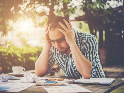 Frustrated Young Man Sitting At Desk With Head In Hands