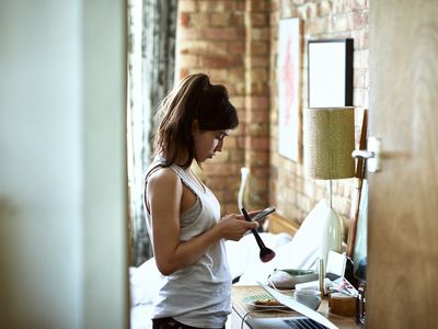 Young woman holding blusher brush and checking smartphone