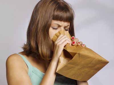 woman having a panic attack using paper bag to calm herself