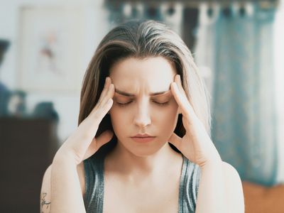 Close-up of a young woman touching head with her eyes closed.