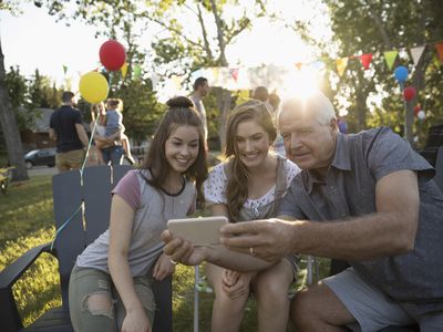 Grandfather and granddaughters taking selfie with camera phone at summer neighborhood block party in park