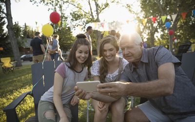 Grandfather and granddaughters taking selfie with camera phone at summer neighborhood block party in park