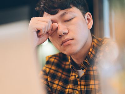 Exhausted young man rubbing eyes in cafe