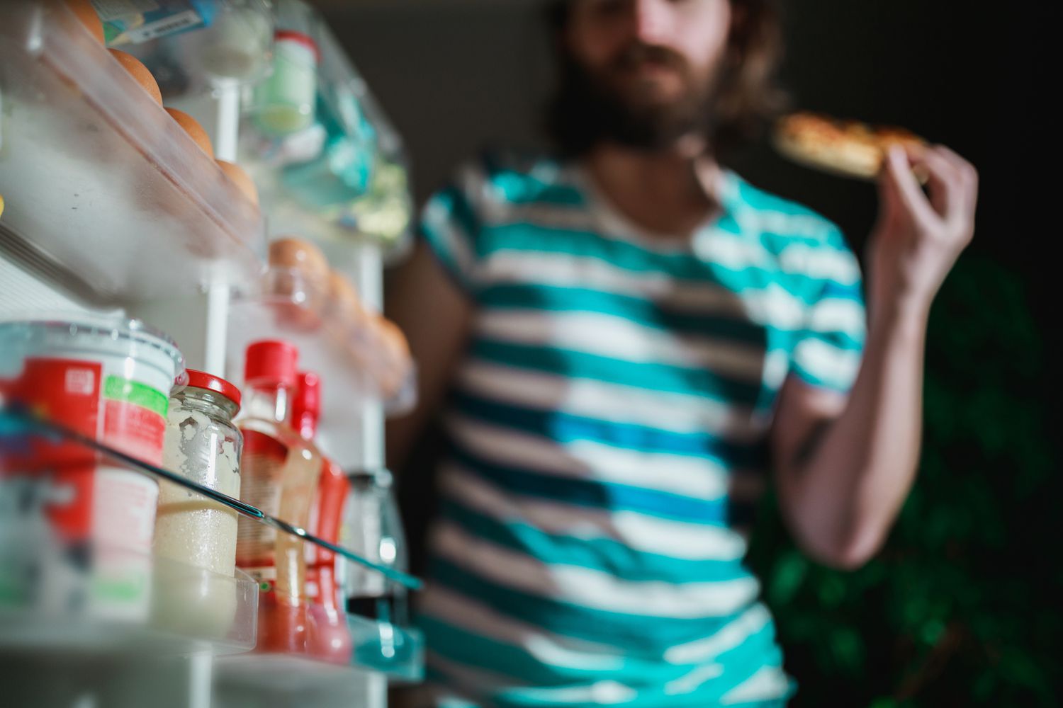 Man eating in front of the refrigerator late night