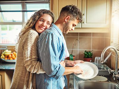 young woman embracing her boyfriend from behind while he does the dishes