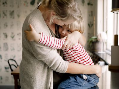 Loving daughter embracing mother while sitting on kitchen counter at home