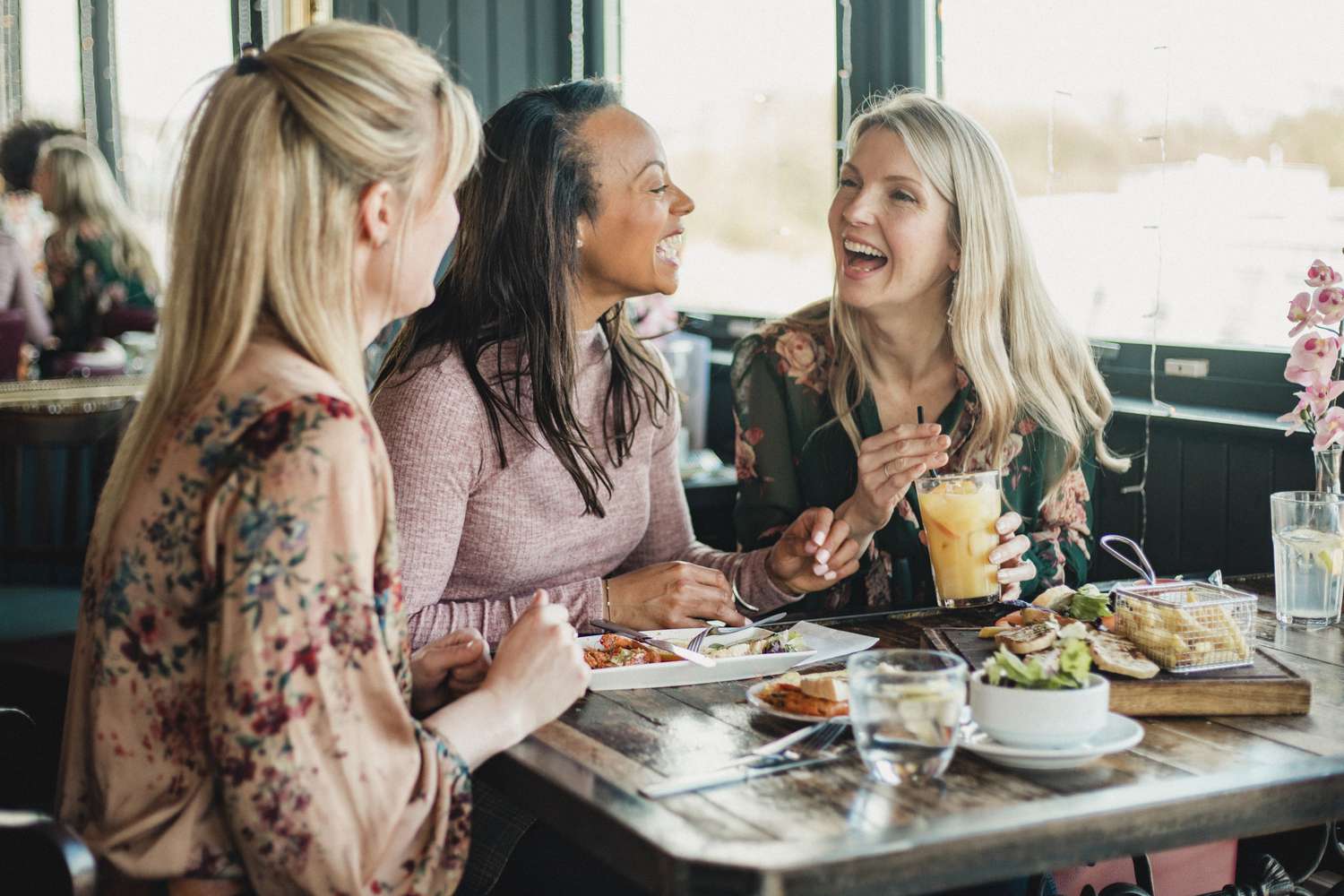 A front view shot of three beautiful mid-adult women enjoying brunch together in a restaurant, they are sitting around a table and laughing with each other.