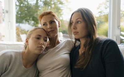 Mother with two teenage girls relaxing on couch at home