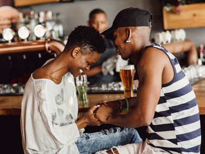  Beautiful smiling and affectionate couple holding hands whilst seated at bar drinking beer