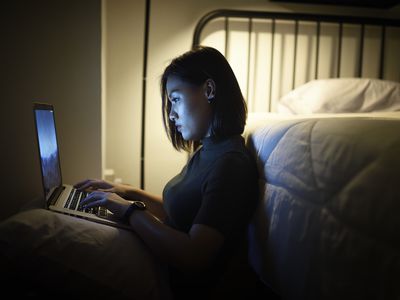 Woman working on her laptop in her bedroom at night 