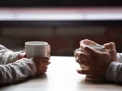 Close up woman and man sitting in cafe, holding warm cups of coffee on table