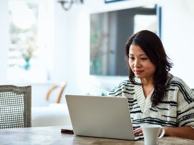 Mid adult woman in her 30s sitting at table and looking at computer, remote working, freelancer, small business