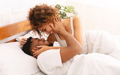 Happy black young couple kissing in bed