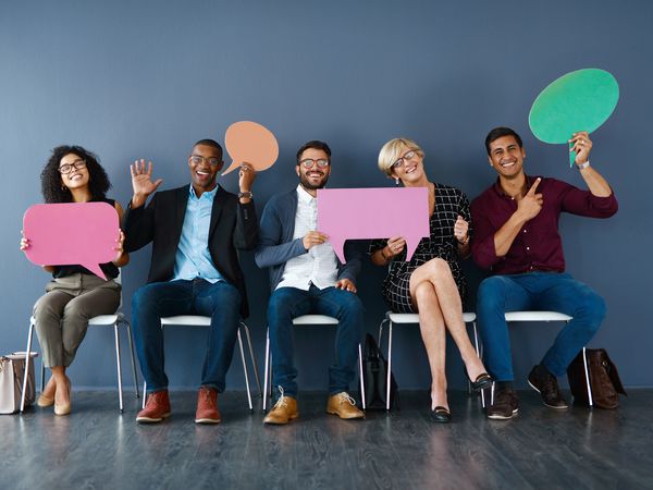 Studio portrait of a group of businesspeople holding speech bubbles while sitting in a row against a grey background