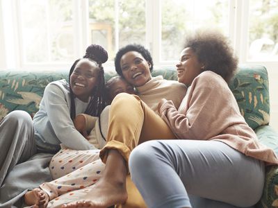 Portrait of happy young woman embracing girls while sitting on sofa at home during Christmas festival