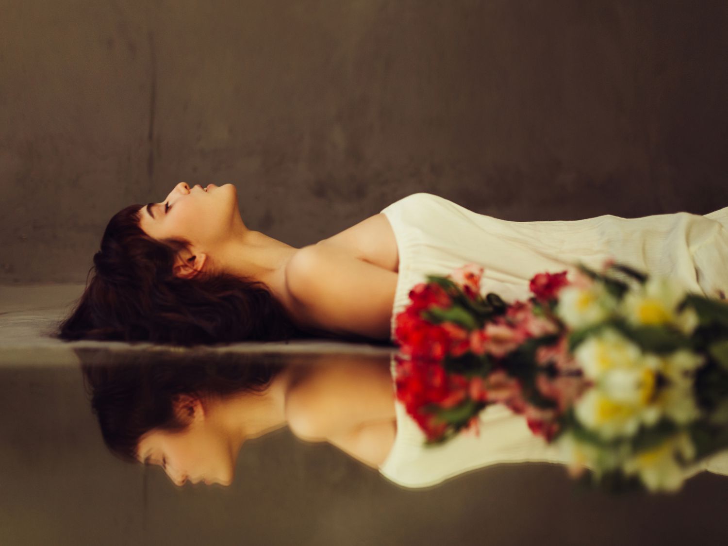 Young woman lying on mirror with flowers