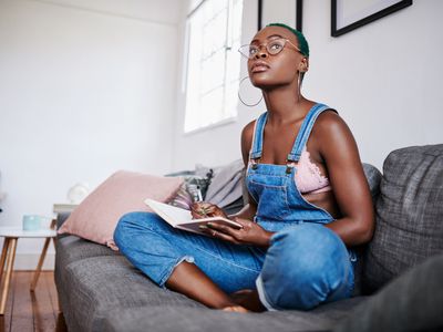 Shot of a young woman writing in a notebook while relaxing on a sofa at home