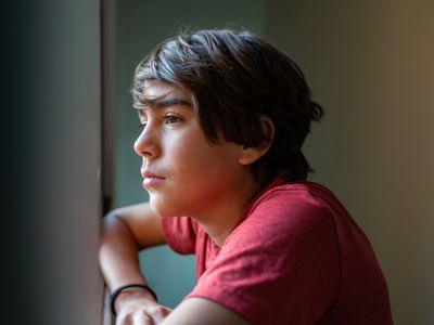 latinx preadolescent boy looking out through window, reflecting, relaxing, pensive