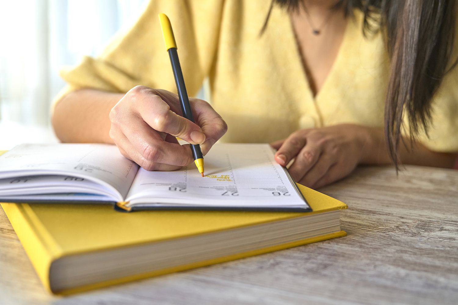 An unrecognizable woman in yellow clothes writes on her datebook