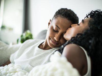 LGBTQ couple at home snuggling under blanket.