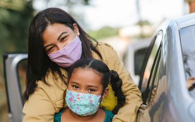 Latinx mom and daughter standing near car.