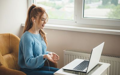 Side view photo of a caucasian woman with red hair and freckles explaining something at laptop wearing earphones