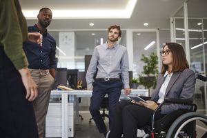 Disabled business woman in wheelchair chatting with coworkers in office