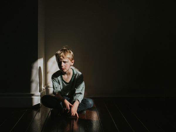 Young boy sits on a dark wooden floor with his legs crossed