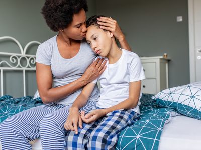 Sad boy is sitting on bed and his mother is hugging and him