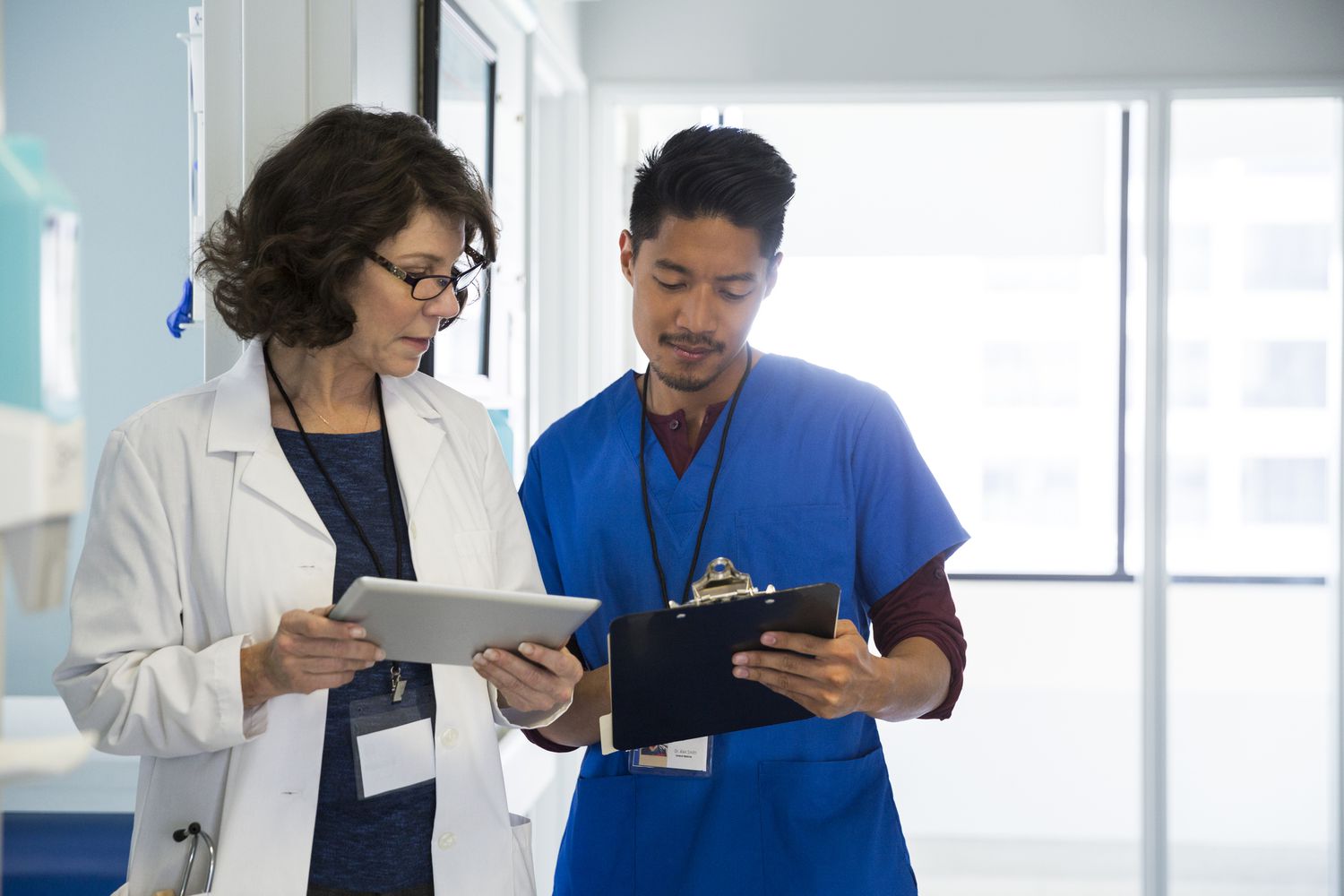 Doctor with male nurse holding digital tablet while discussing in mental hospital corridor 