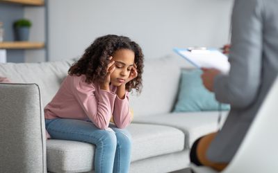 Unhappy girl listening to psychologist at meeting, thinking about her problems