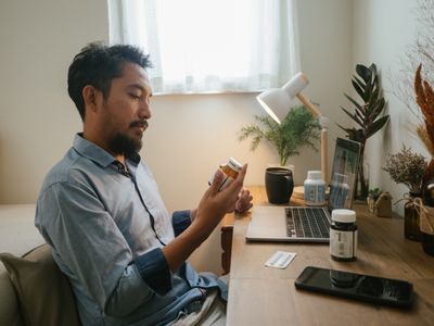 Asian man looking at pill bottle and listening to women doctor in consultation medicine to video conference at home.