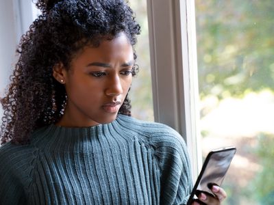 African American female stares outside her window looking cellphone.