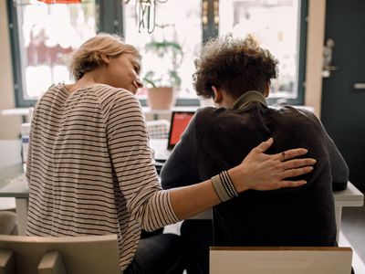 Mother sitting by teenage son studying at home 