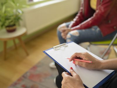 Close up of a psychologist notes and a students knees during a mental health meeting in a stylish office