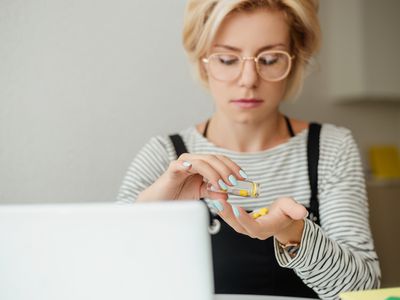 Defocused young woman in eyeglasses pouring out pills from glass bottle on hand.