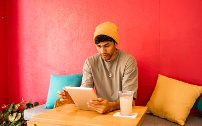 Young Latin student using digital tablet for studying . He is having a soda drink while working