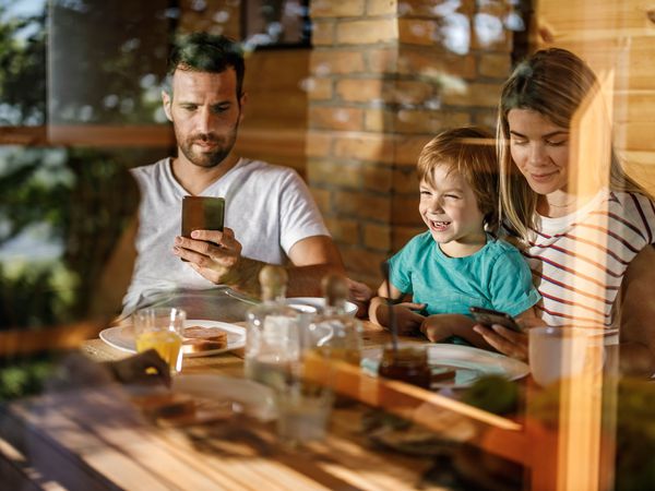 Careless parents using their smart phone while having breakfast with their kids in dining room